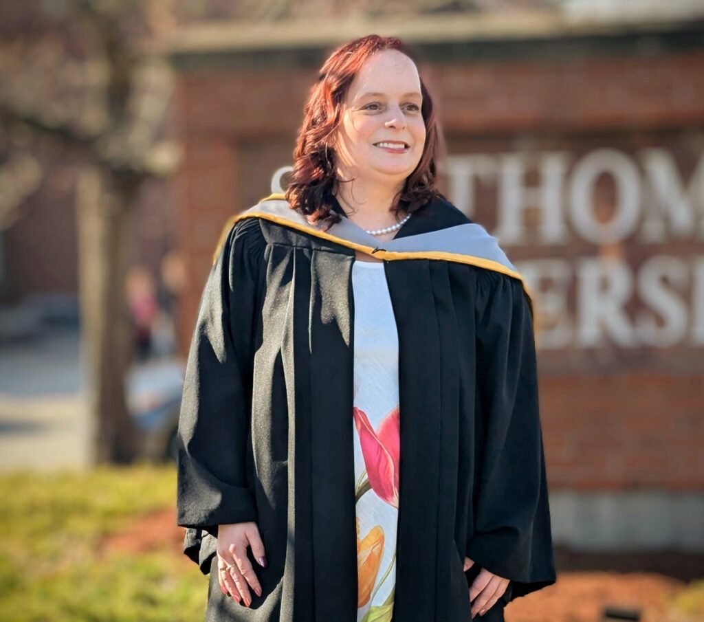 Elizabeth Doherty is a woman with long red hair. She is smiling while standing in her graduation gown.