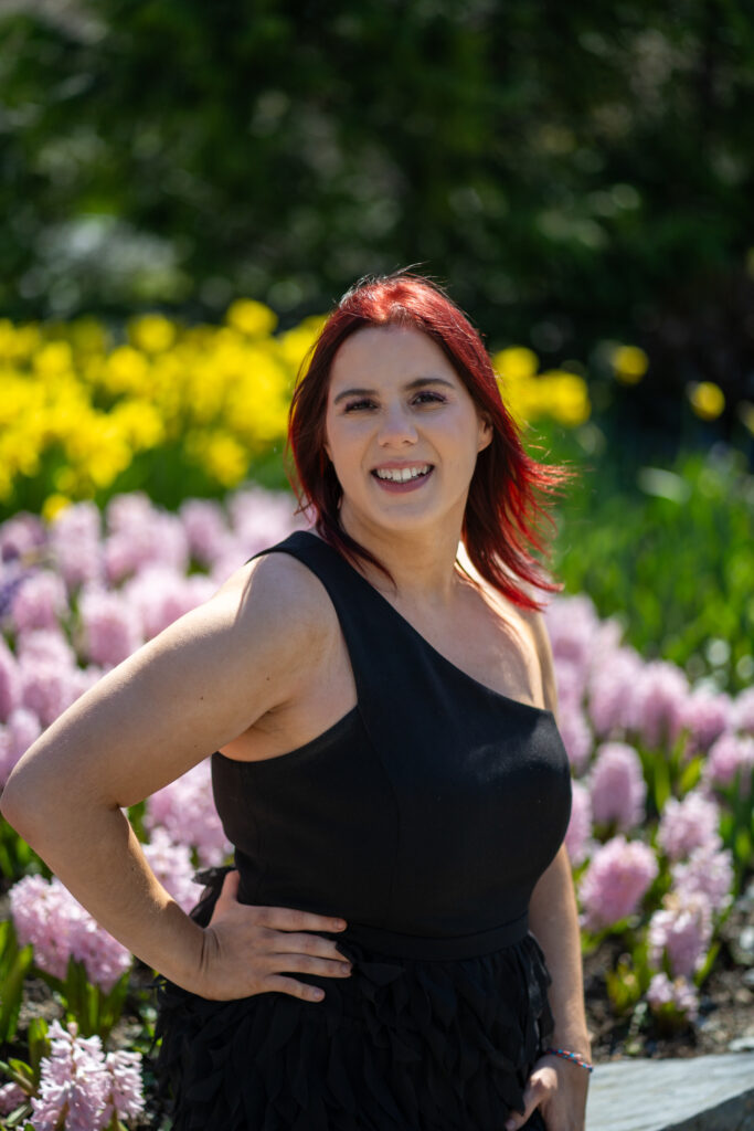Stephanie Evans is a woman with long red hair. She is wearing a black dress and standing with her hand on her hip.