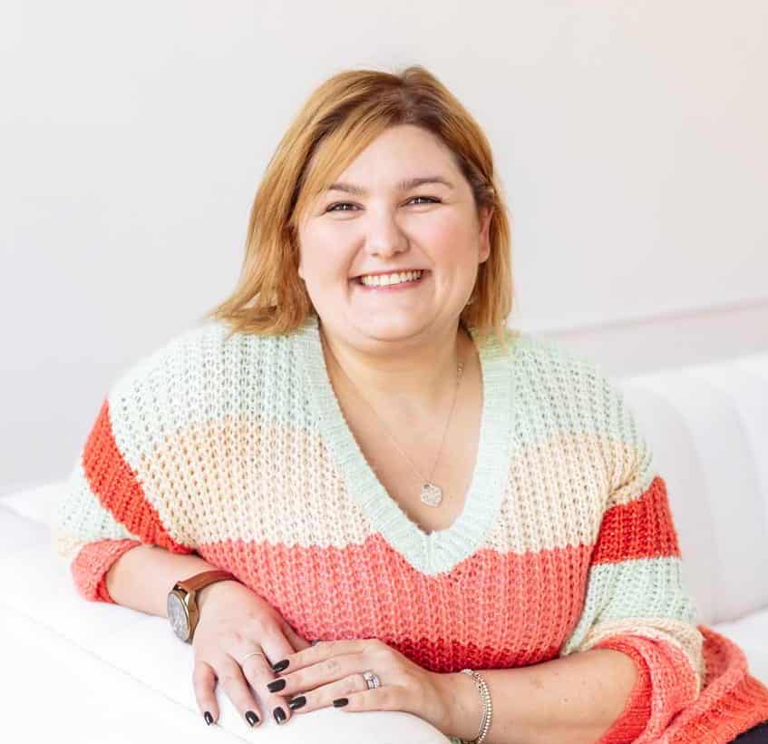 Matisse sits on a white couch smiling at the camera.