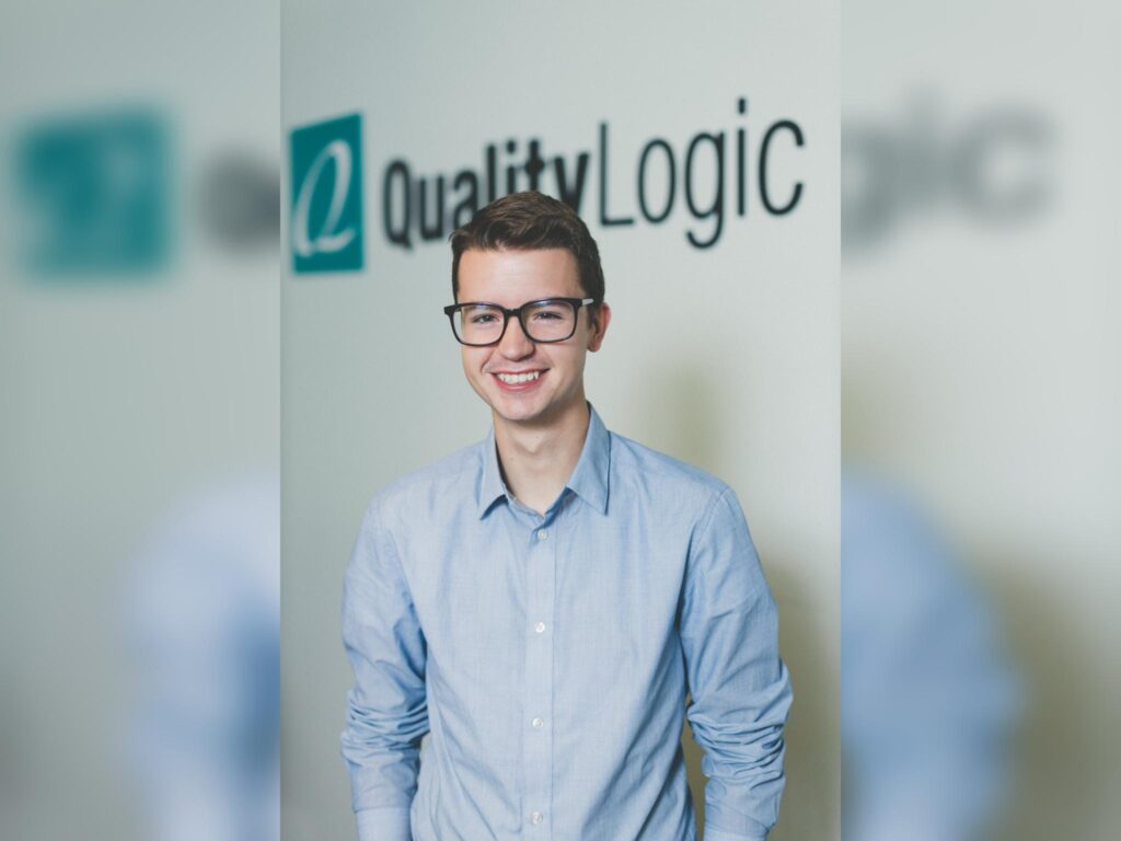 Clyde Valentine, a young man with large, dark-rimmed glasses and blue shirt, stands in front of a Quality Logic logo.