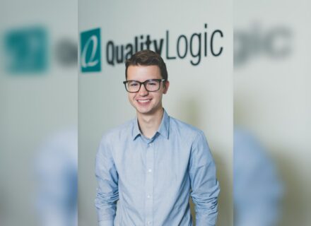 Clyde Valentine, a young man with large, dark-rimmed glasses and blue shirt, stands in front of a Quality Logic logo.