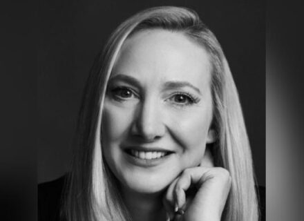 A black and white photo of Joanne Henry, a woman with long blonde hair, resting with her hand on her chin.