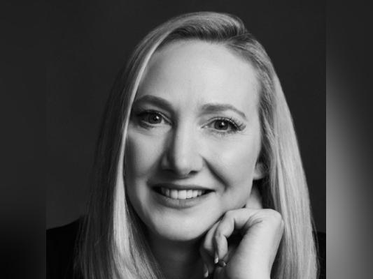 A black and white photo of Joanne Henry, a woman with long blonde hair, resting with her hand on her chin.